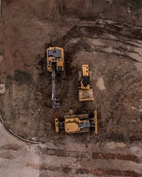 Home An aerial shot of heavy machinery at a construction site, including excavators and road rollers.