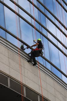 Home A window cleaner using ropes on a modern skyscraper in daylight.