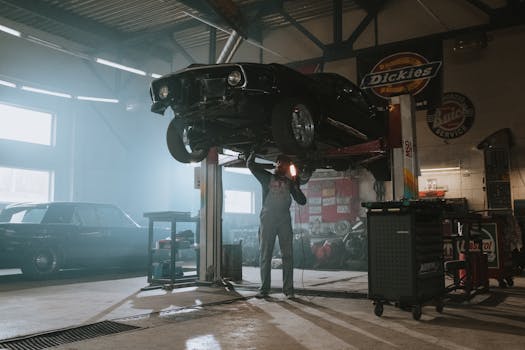 Home Male mechanic using a light to inspect a classic car lifted in an automotive garage.